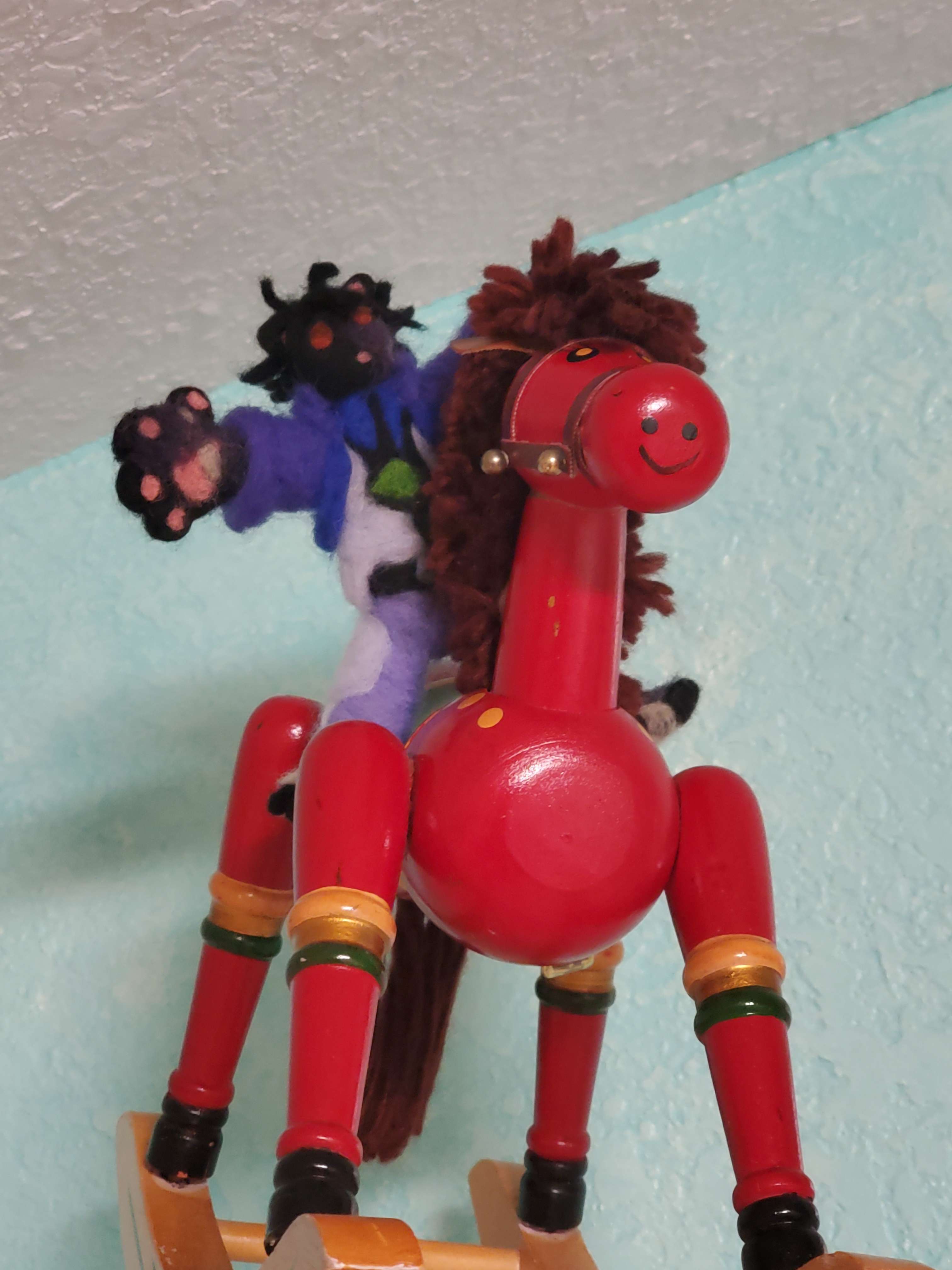 felted black cat wearing a blue suit sitting on top of a red rocking horse